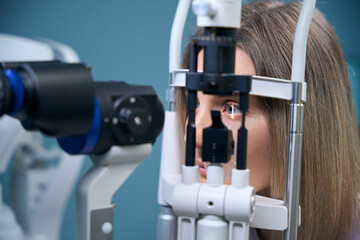 Young woman examining her eyes with a measurement machine in ophthalmology center