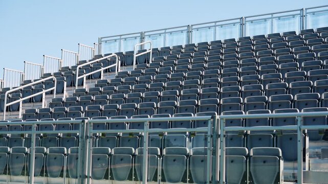 Empty bleacher seating under a clear blue sky with white railings and modern glass barriers