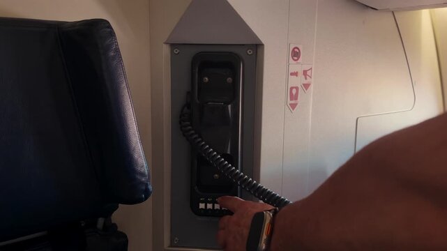 Close-up view of the hand of a mali caucasian caib crew menber grabbing the Emergency intercom handset. He is wesring leather bracelets.