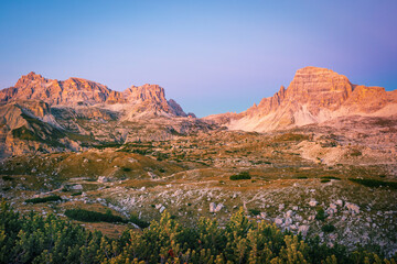 Obraz premium Tre Cime di Lavaredo in the Dolomites, Italian Alps, with dramatic jagged peaks illuminated by side sunlight and contrasted against a stormy sky. Panoramic alpine scenery with rocky cliffs and rugged 