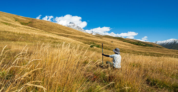 Hiker sitting in grass and resting while admiring Mount Ushba near Mestia, Svaneti, Georgia. Peaceful moment in nature.