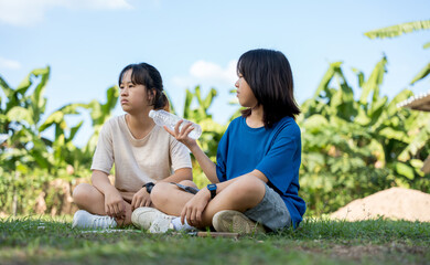 Two girls sitting on grass, one offering a water bottle after playing badminton.