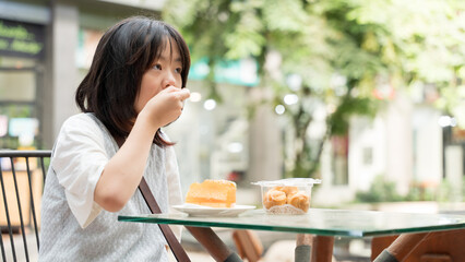 A girl enjoying a bite of dessert at an outdoor cafe surrounded by greenery.
