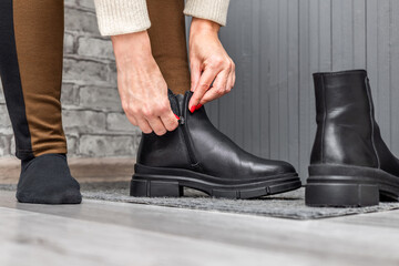 a woman puts on boots, close-up. A woman zips up her black boots. The girl puts on black leather boots. a woman unfastens her boot © Oleg Opryshko