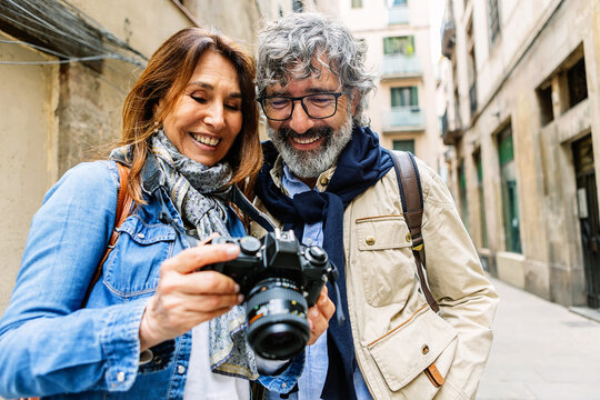 Smiling senior couple reviewing photos on camera in Barcelona. Mature pair enjoying captured memories while sightseeing together. Travel and lifestyle concept.