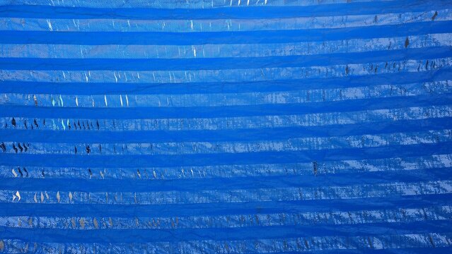 Old damaged blue tarp texture with dirt and rips. Texture of a weathered blue plastic tarp featuring dirt stains and torn edges from usage and age.