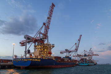 Container vessels beneath giant port cranes at dusk