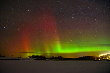 Colorful aurora borealis over snowy fields and trees beneath a bright starry night sky.