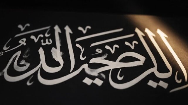 White Arabic calligraphy on dark background illuminated by warm light