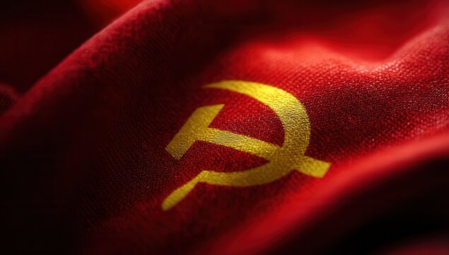 Red flag with yellow hammer and sickle symbol representing communist ideology in a close-up view captured indoors