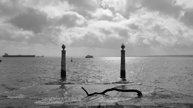 Black and white view of the historic Cais das Colunas pier in Lisbon, Portugal, featuring the two stone columns on the Tagus River. 