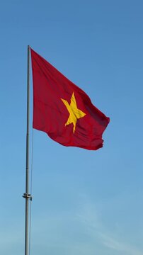Vertical slow motion view of Vietnam flag waving smoothly in the wind, isolated against a clear open blue sky. Civic identity.