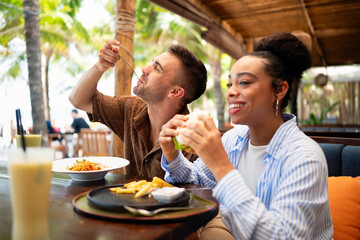Multiethnic couple enjoying a joyful dining experience by the beach. Great food, perfect summer vibe