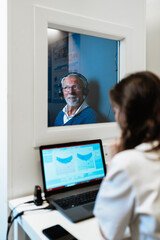 An elderly man wearing headphones takes a professional hearing assessment inside a soundproof booth...
