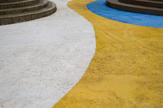 Abstract curved outdoor pavement with white, yellow and blue painted stripes and concrete steps. Modern urban geometric background with texture, bold color contrast and copy space.
