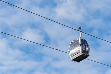 A silver cable car is suspended in the air. The cable car is on a wire that is attached to a pole