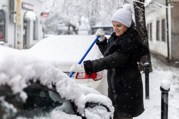 Woman clearing snow from car windshield on winter day