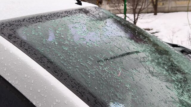 Icy rain falls on a frozen car windshield covered with ice crystals: winter damage