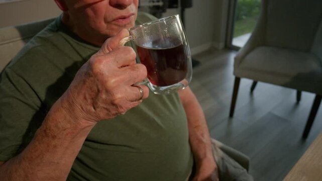 elderly man enjoys a late day cup of coffee, blowing on it to cool the hot liquid down, caffeine to end the day