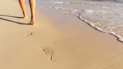 Woman enjoying summer vacation by walking barefoot on sandy beach near the ocean as waves wash up, focus on footprint in the sand © Home-stock