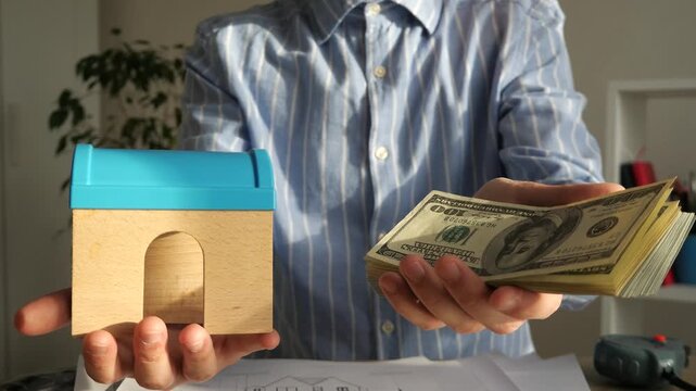 A powerful visual metaphor for investment and tangible assets. This striking close-up shows a businessman presenting money in one hand and a miniature house model in the other, symbolizing capital
