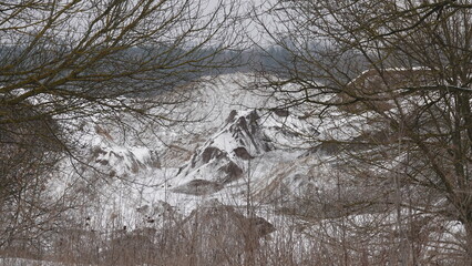 Góra piasku pokryta śniegiem widoczna za nagimi gałęziami w okresie zimowym © tomo81