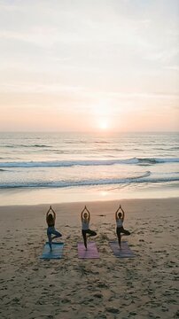 Group of women meditating in lotus pose on the sand at the beach during sunrise. Team yoga, peaceful, morning routine, meditation, outdoor.
