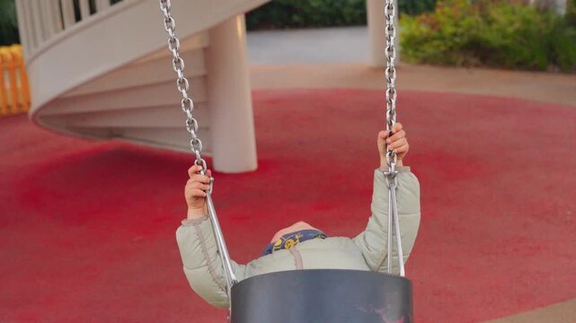 Unhappy Asian boy swinging on a swing set at an outdoor playground