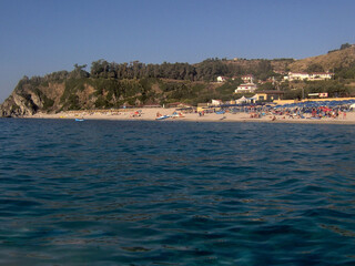 Beautiful panoramic view of the Calabrian coast during the summer season, featuring turquoise crystal-clear waters, dramatic rocky cliffs, and charming seaside scenery under bright blue skies. The