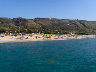 Beautiful panoramic view of the Calabrian coast during the summer season, featuring turquoise crystal-clear waters, dramatic rocky cliffs, and charming seaside scenery under bright blue skies. The
