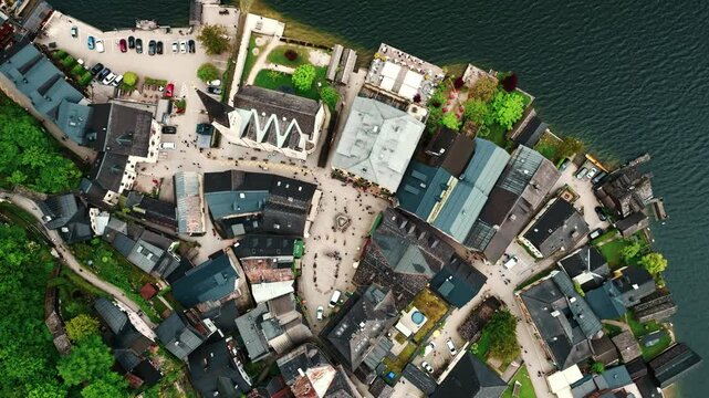 Aerial drone footage of Hallstatt, Austria, showing the picturesque alpine village, lake shoreline, historic buildings, and surrounding mountains.