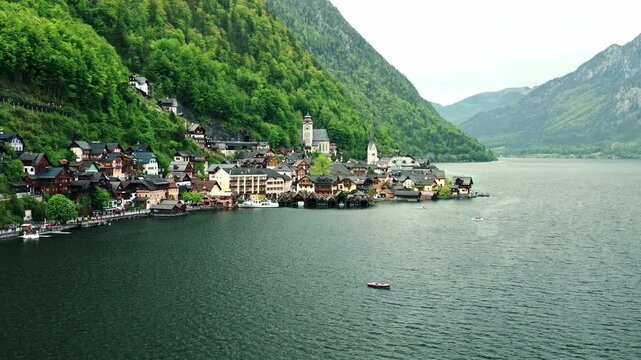 Aerial drone footage of Hallstatt, Austria, showing the picturesque alpine village, lake shoreline, historic buildings, and surrounding mountains.