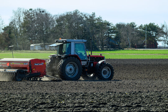 Falkenberg, Sweden, april 4-2025: A tractor is plowing a dark, freshly worked field on a sunny day. The vehicle is equipped with a seed drill, preparing the soil for crops