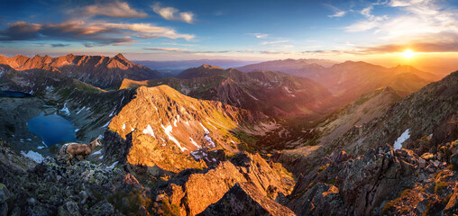 Snow covered mountain landscape with alpine peaks, rocky cliffs and pine trees under a dramatic...