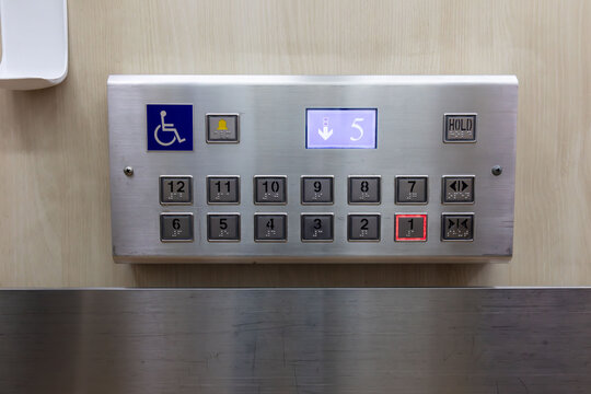 A silver elevator control panel with a blue disable sign. braille signage on elevator buttons.