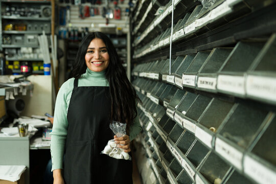 Latin woman working in hardware store holding small parts, smiling while helping customers with diy projects
