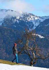 Senior woman hiking in winter near Oberstaufen, enjoying warm afternoon sunlight and a panoramic snowy mountain landscape in the Allg&auml;u region of Bavaria, Germany.