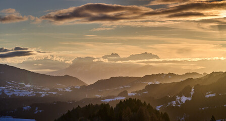 Alpine winter landscape in Bregenzer Wald at sunset with snow-covered mountains and Saentis summit  glowing in warm evening light under a dramatic sky. Austria, Vorarlberg