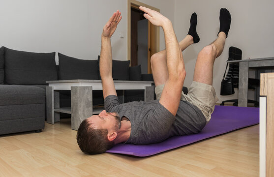 A young man does the dead bug core exercise in his living room to stabilize his spine. Healthy lifestyle, exercising at home