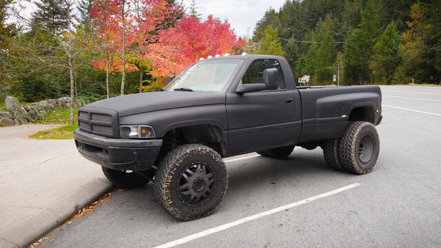 1996 Dodge Ram 3500 dually with large tires parked in a empty parking area with multi-coloured trees in the background.