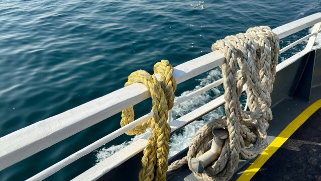 "Coiled nautical ropes on a ship railing with the sea in the background. Close-up of yellow and white marine cords on a boat deck during a Bosphorus cruise in Istanbul, Turkey."