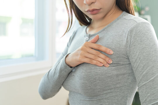 Health care breast cancer checking concept. Asian young woman, girl doing self check of breast cancer on gray t-shirt in room at home on white wall. How do I check breast cancer prevention awareness.