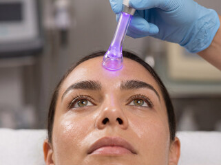 Naklejka premium High Frequency Facial Treatment. Woman Receiving Electric Current Skin Therapy with Violet Wand at Spa.
