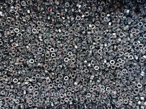 Top view background of a large group of silver metallic hex nuts. This industrial hardware texture features shiny steel fasteners, perfect for themes related to construction, mechanical engineering, a