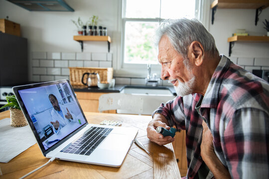 Senior man consulting doctor via telehealth at home kitchen table