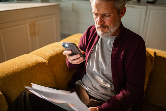 Middle-aged man scanning bills with smartphone at home