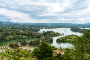 Lush green landscape with winding lake, small islands and mountains under cloudy skies seen from Piedra del Pe&ntilde;ol in Guatape near Medellin, Colombia