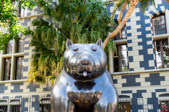Medellin, Colombia - November 21, 2025: Bronze sculpture by renowned Colombian artist Fernando Botero stands in front of the iconic Rafael Uribe Uribe Palace of Culture, surrounded by lush green trees