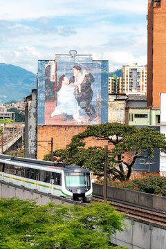 Medellin, Colombia - November 21, 2025: Daytime view of downtown Medellin featuring a colorful Fernando Botero mural, a metro train in motion, the historic Rafael Uribe Uribe Palace of Culture