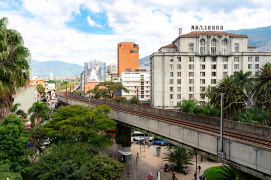 Medellin, Colombia - November 21, 2025: Wide cityscape of central Medellin, Colombia, showing the elevated metro line, the iconic Hotel Nutibara, palm trees, and the Andean mountains under partly clou